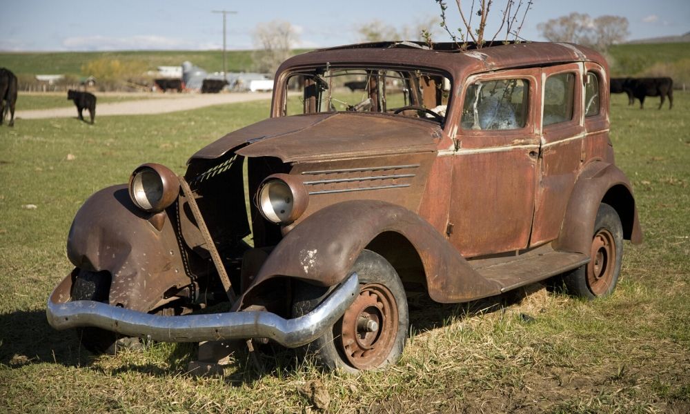 A old, rusted car in a farm field.