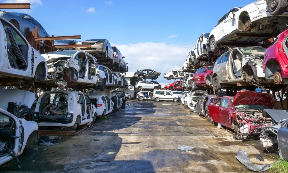 Many cars piled on top of each other in a junk yard.