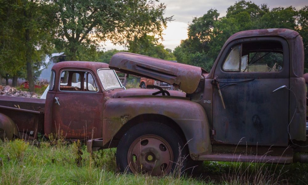 Two older, broken-down cars in a field.