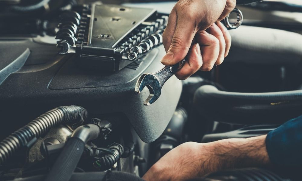 A person with a wrench in his/her hand repairing the engine of a car.