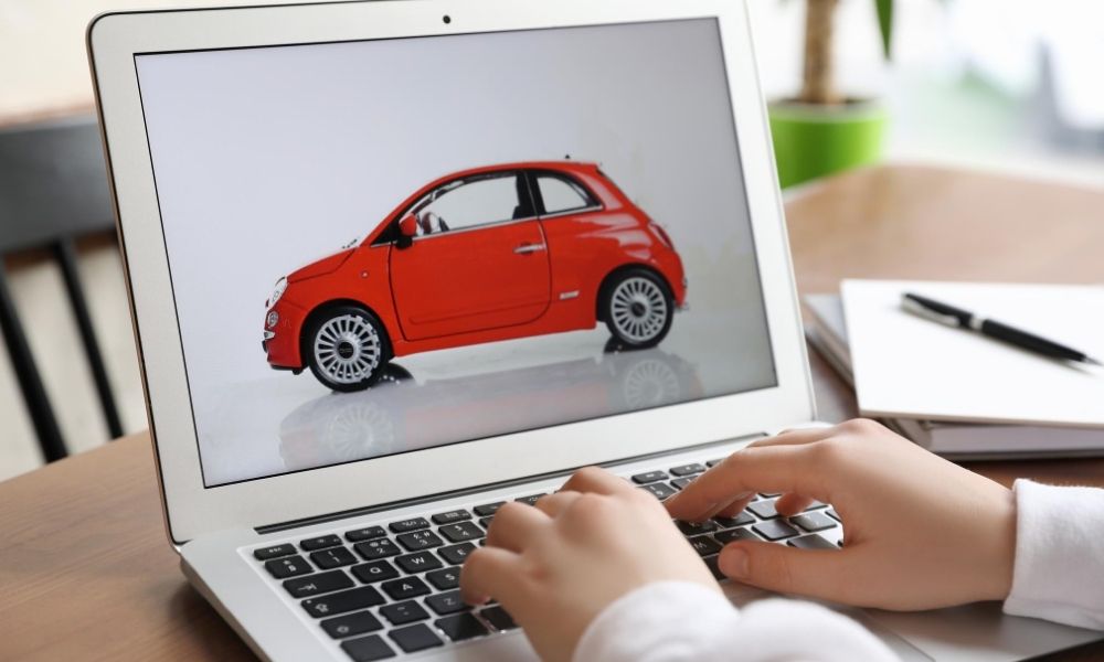 A set of hands typing at a laptop viewing a car online.