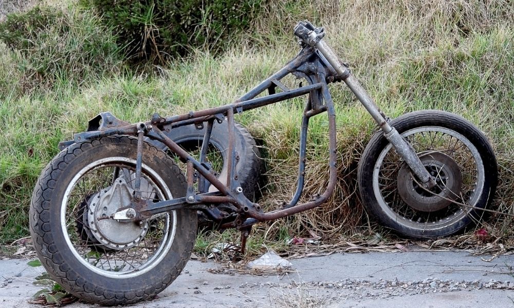 An abandoned motorcycle near a foresty trail.