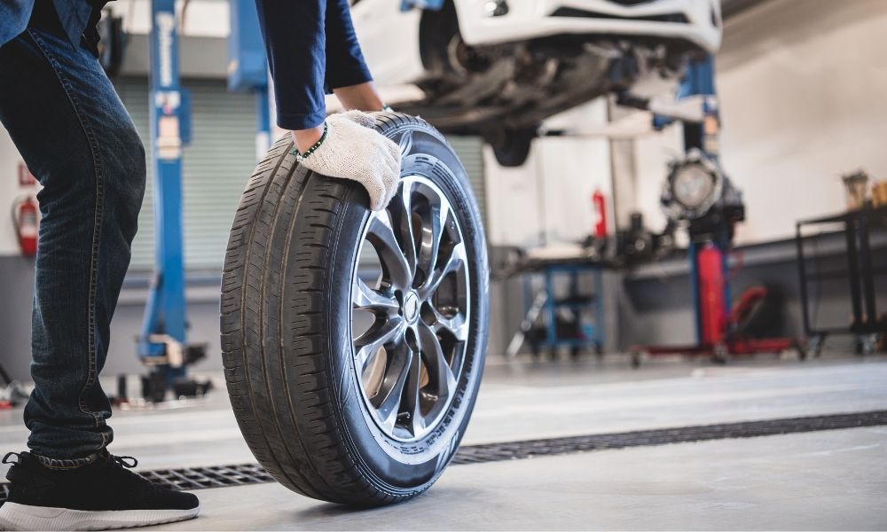 A tire technician rolling a tire on a shop floor.