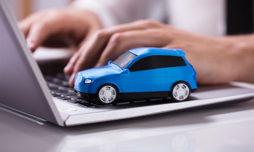 A person typing on a laptop with a toy car placed on the laptop.